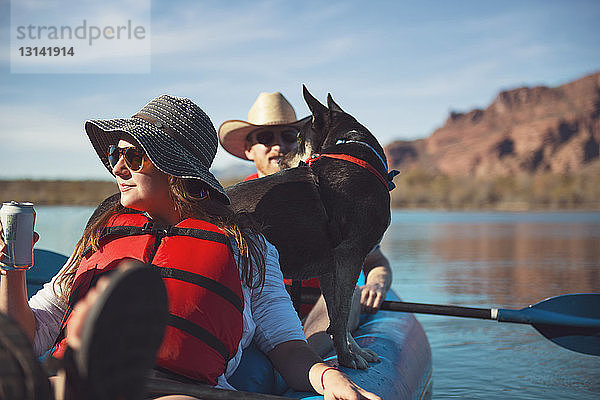 Freunde mit Hund sitzen im aufblasbaren Kajak auf dem See