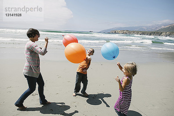 Mutter und Kinder spielen mit Luftballons  während sie am Strand im Sand stehen