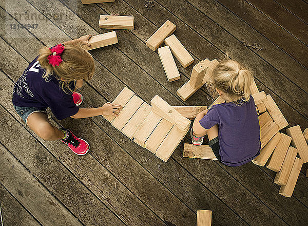 Hochwinkelansicht von Schwestern  die mit Holzspielzeugblöcken spielen  während sie auf dem Boden kauern