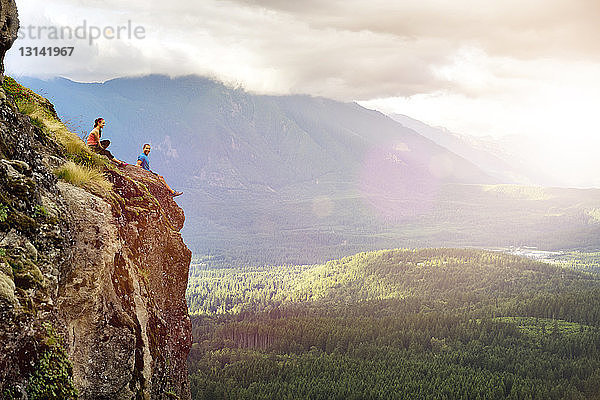 Seitenansicht eines Paares  das auf einer Klippe gegen einen Berg sitzt