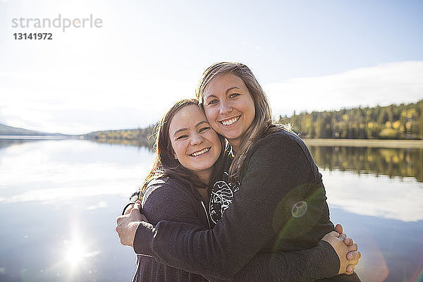 Porträt von fröhlichen Freundinnen  die sich bei Sonnenschein am See umarmen