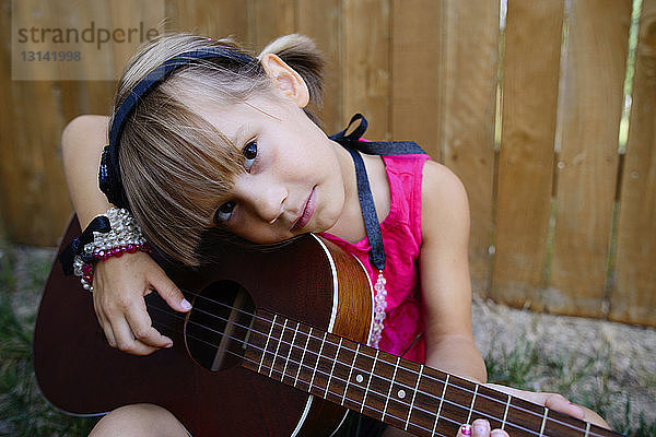 Porträt eines Gitarre klimpernden Mädchens  das an einem Holzzaun sitzt