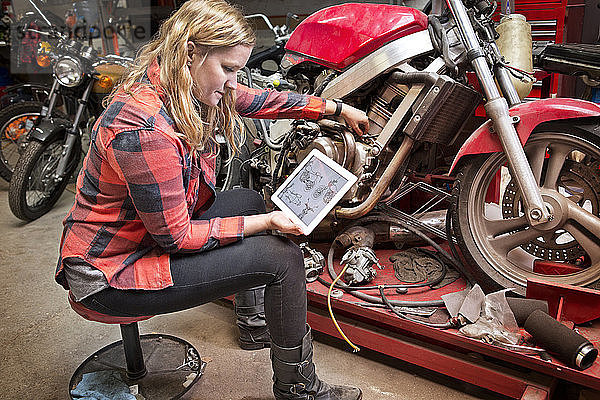 Hochwinkelaufnahme einer Frau  die ein digitales Tablett zur Reparatur ihres Fahrrads in der Werkstatt verwendet