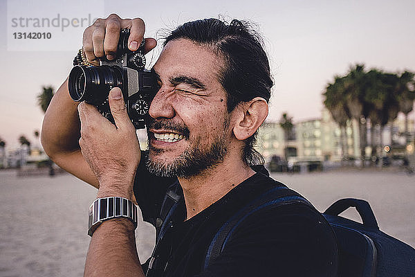 Nahaufnahme eines Rucksacktouristen  der mit der Kamera am Strand fotografiert