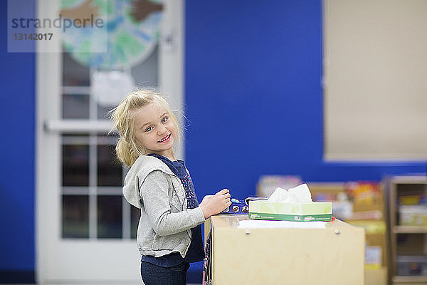 Porträt eines niedlichen lächelnden Mädchens  das in der Schule am Tisch steht