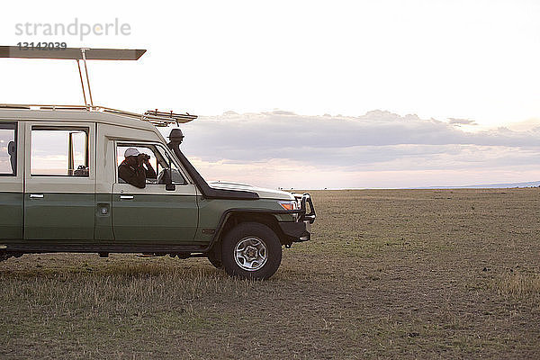 Mann schaut durch ein Fernglas  während er im Geländewagen im Serengeti-Nationalpark sitzt