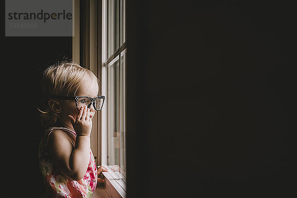 Mädchen mit Brille beim Blick durchs Fenster