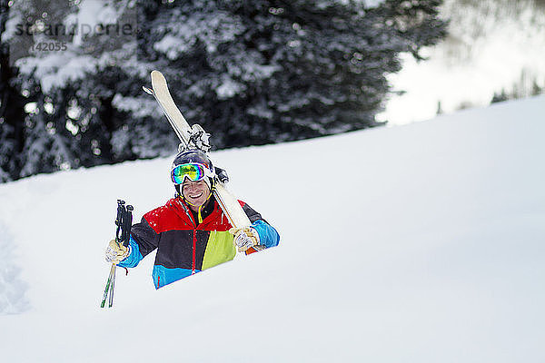 Fröhlicher Mann mit Skiern beim Gehen auf schneebedecktem Feld