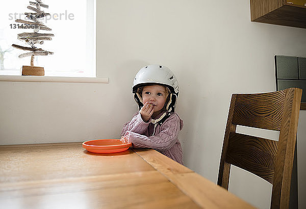 Mädchen mit Helm isst zu Hause am Tisch