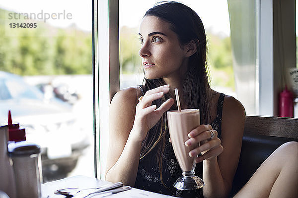 Frau schaut weg  während sie einen Schoko-Milchshake im Café hält