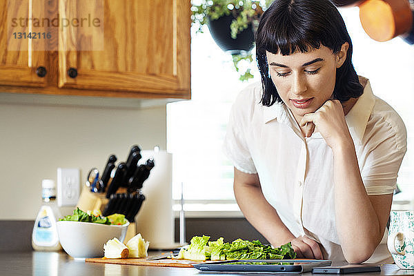 Lächelnde Frau liest digitale Tablette beim Zubereiten von Essen in der heimischen Küche