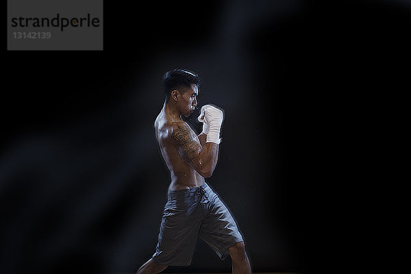 Seitenansicht eines männlichen Kickboxers  der vor schwarzem Hintergrund kämpft