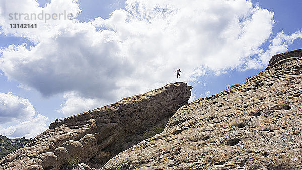 Fernansicht eines Mannes  der auf Felsformationen gegen bewölkten Himmel springt