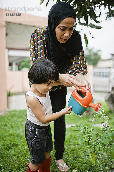 Mutter mit Sohn gießt Pflanzen im Garten