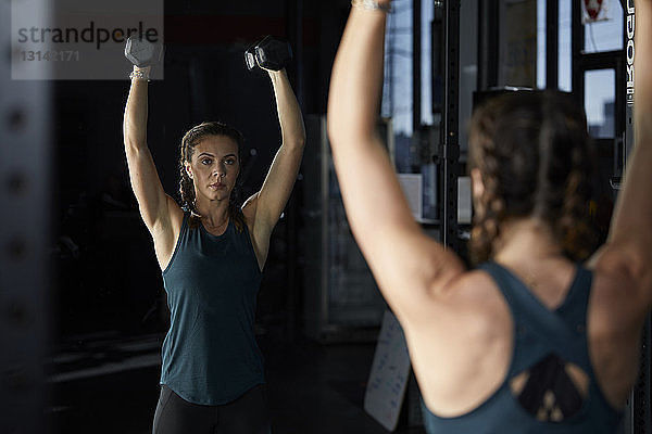 Reflektion einer Frau  die Hanteln im Fitnessstudio hebt  im Spiegel gesehen