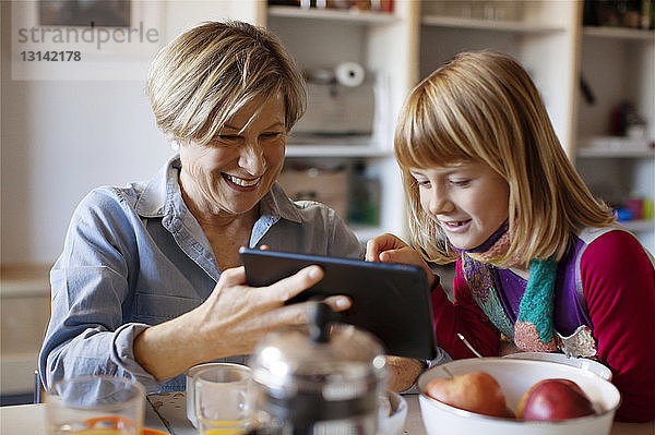 Großmutter zeigt Enkelin Tablet-Computer  während sie am Tisch sitzt