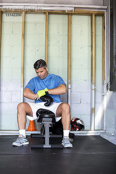 Männlicher Boxer trägt Boxhandschuhe beim Sitzen in der Turnhalle