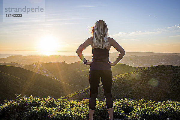 Rückansicht einer Frau  die bei Sonnenuntergang am Berg trainiert