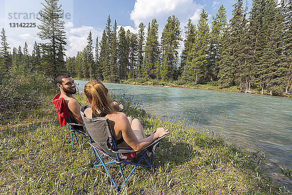 Freunde unterhalten sich  während sie auf Stühlen am Flussufer im Banff-Nationalpark sitzen