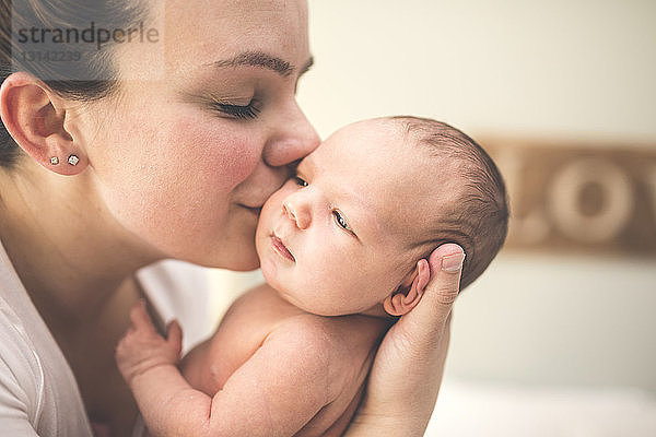 Seitenansicht einer Mutter  die ihre neugeborene Tochter zu Hause küsst