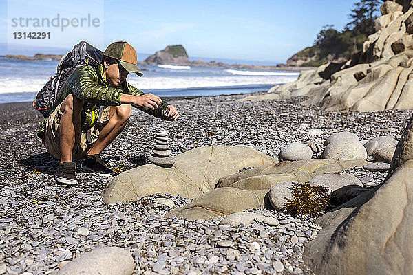 Teenager stapelt Steine am Meeresufer am Strand