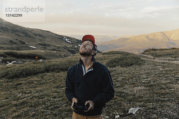 Mann schaut auf  während er die Fernsteuerung der Drohne gegen Berge einsetzt