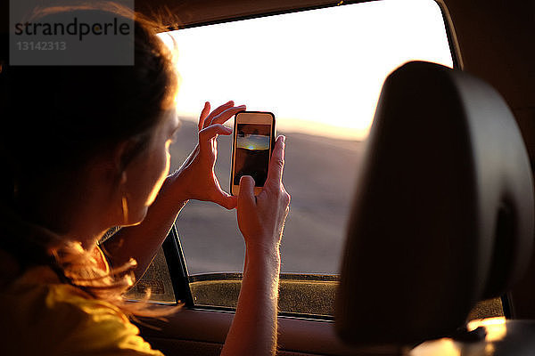 Frau im Auto fotografiert den Himmel bei Sonnenuntergang