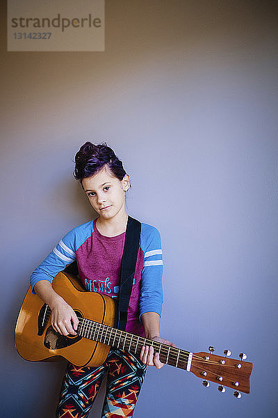 Porträt eines Gitarre spielenden Mädchens  das zu Hause an der Wand steht