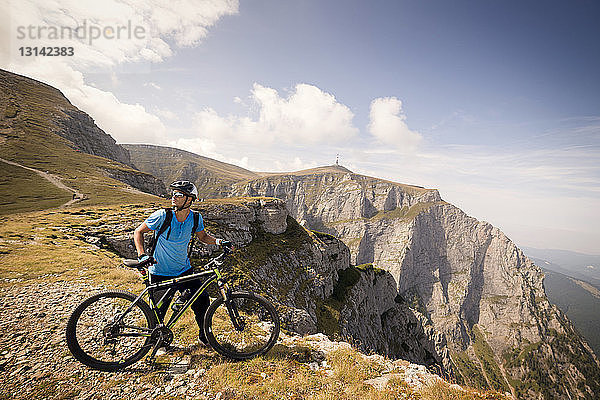 Männlicher Radfahrer schaut weg  während er mit dem Fahrrad auf dem Berg steht