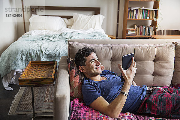 Lächelnder Mann benutzt Tablet-Computer  während er zu Hause auf dem Sofa liegt