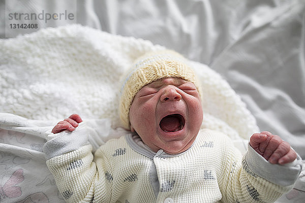 Draufsicht auf ein süßes neugeborenes Mädchen  das weint  während es zu Hause im Bett liegt