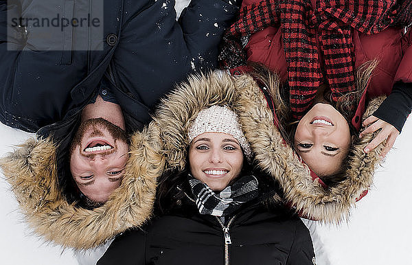 Hochwinkelporträt von lächelnden Freunden  die auf einem schneebedeckten Feld liegen