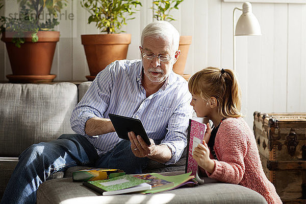 Großvater zeigt Enkelin beim Entspannen zu Hause einen Tablet-Computer