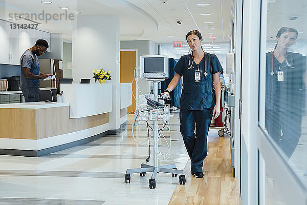 Porträt einer selbstbewussten Ärztin bei der Überwachung von Geräten  wobei die Kollegin am Krankenhausempfang steht