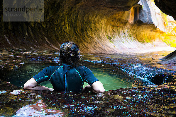 Rückansicht einer Frau  die sich im Teich an einer Felsformation entspannt