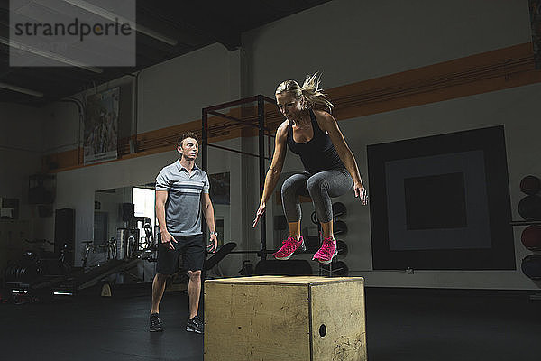 Trainer betrachtet Kunden  die im Fitnessstudio auf die Box springen