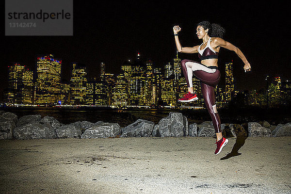 Weibliche Athletin springt nachts gegen beleuchtete Gebäude