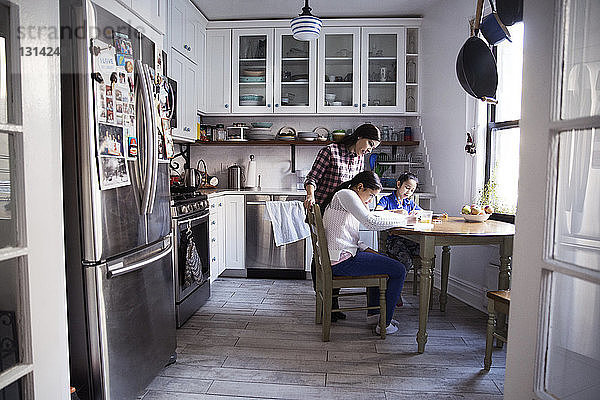 Frau hilft Töchtern beim Lernen am Tisch in der Küche