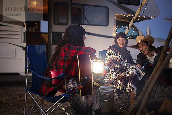 Freunde genießen beim Camping gegen Wohnmobil in der Nacht