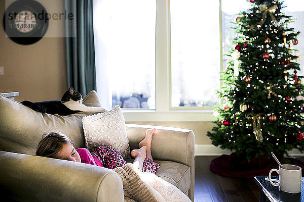 Mädchen schläft zu Hause auf dem Sofa am Weihnachtsbaum