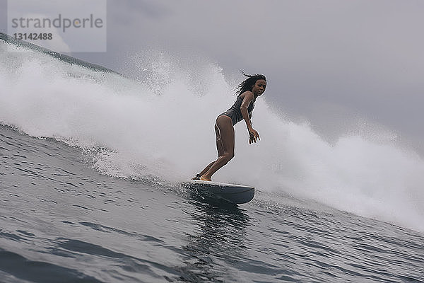 Seitenansicht einer Frau im Taucheranzug beim Surfen auf dem Meer vor bewölktem Himmel