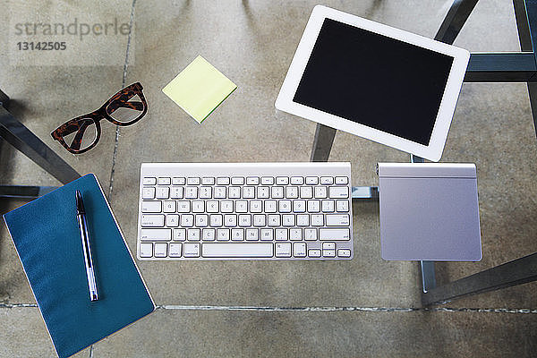 Draufsicht eines Tablet-Computers mit Tastatur und Touchpad auf einem Glastisch im Kreativbüro