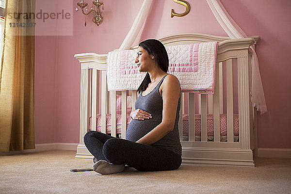 Schwangere Frau sitzt zu Hause auf dem Boden am Kinderbett
