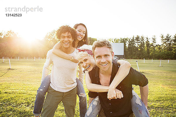 Porträt von lächelnden Männern  die Freunde auf dem Spielfeld huckepack nehmen