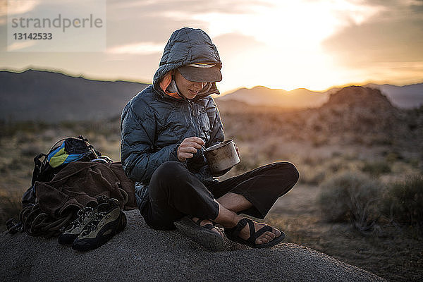Glückliche Wanderin isst Essen  während sie auf einer Sanddüne sitzt
