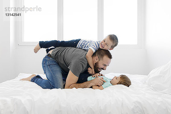 Verspielter Vater spielt zu Hause mit den Söhnen im Bett