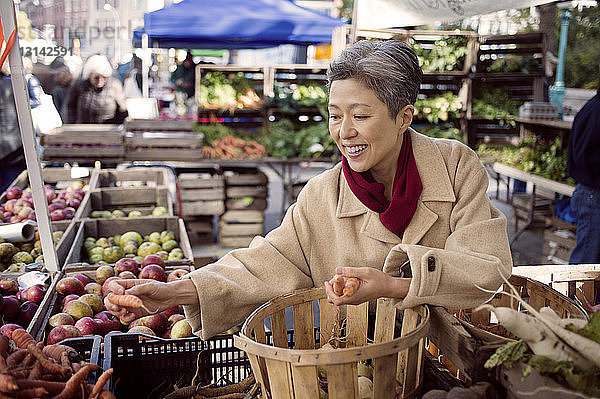 Glückliche reife Frau kauft Gemüse auf dem Bauernmarkt
