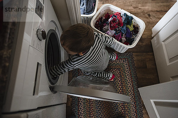 Schrägaufnahme eines Jungen  der zu Hause Wäsche in die Waschmaschine steckt