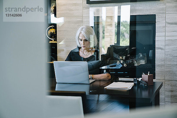 Seriöse Geschäftsfrau  die am Laptop im Büro arbeitet  durch die Tür gesehen