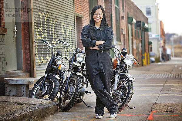Porträt einer glücklichen Mechanikerin  die vor dem Geschäft gegen Fahrräder steht